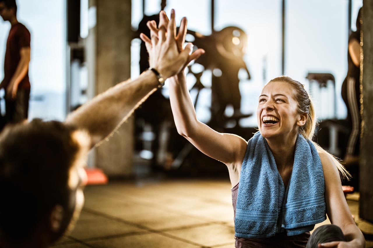 Happy female athlete having fun while giving her trainer high-five on a break in a gym.