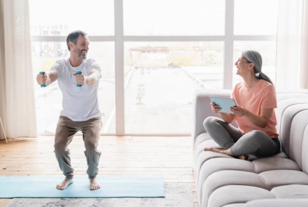A middle-aged couple keeping fit at home using a technological device.